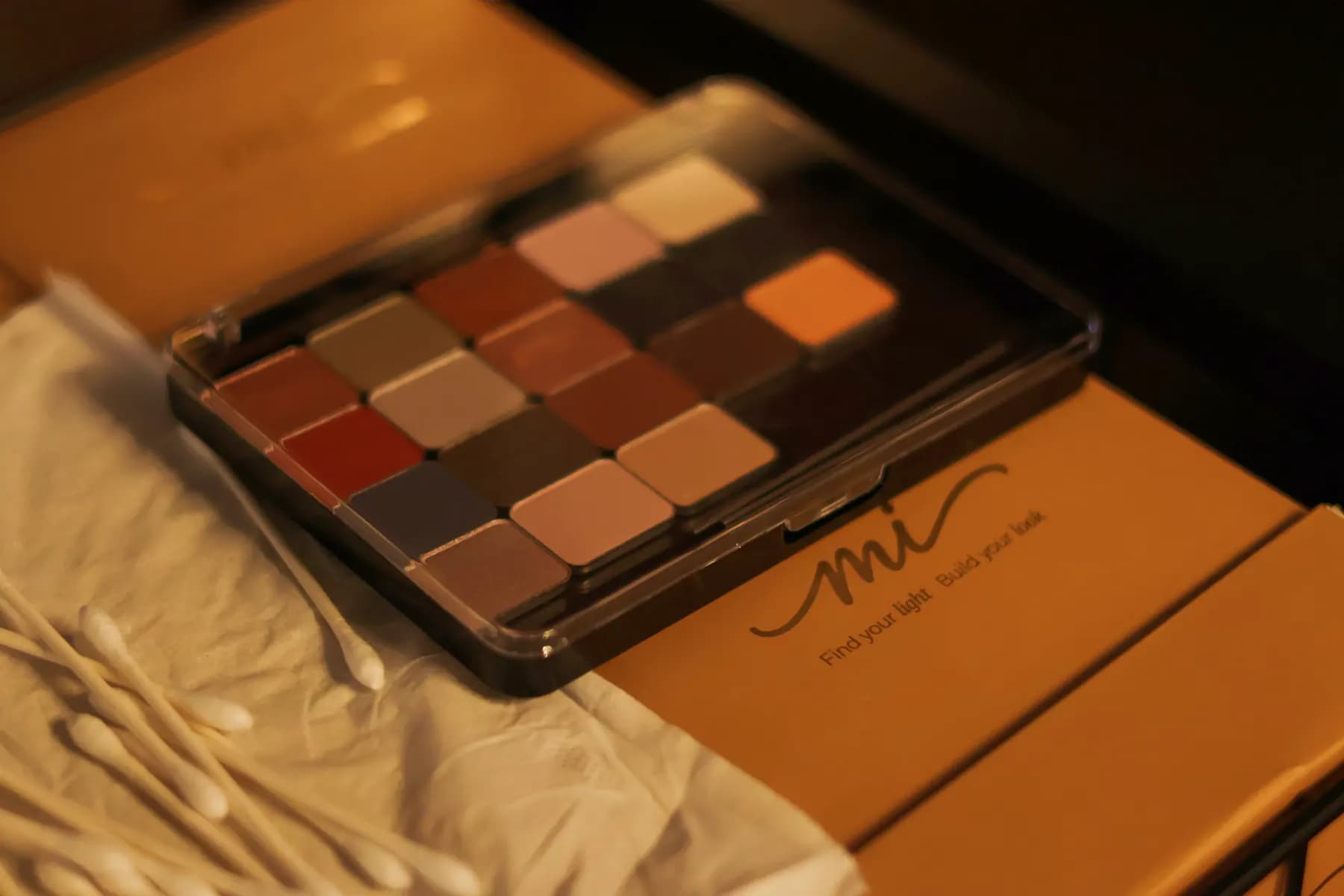A custom MiPalette case filled with warm neutral and bold refill shades rests on its branded box.