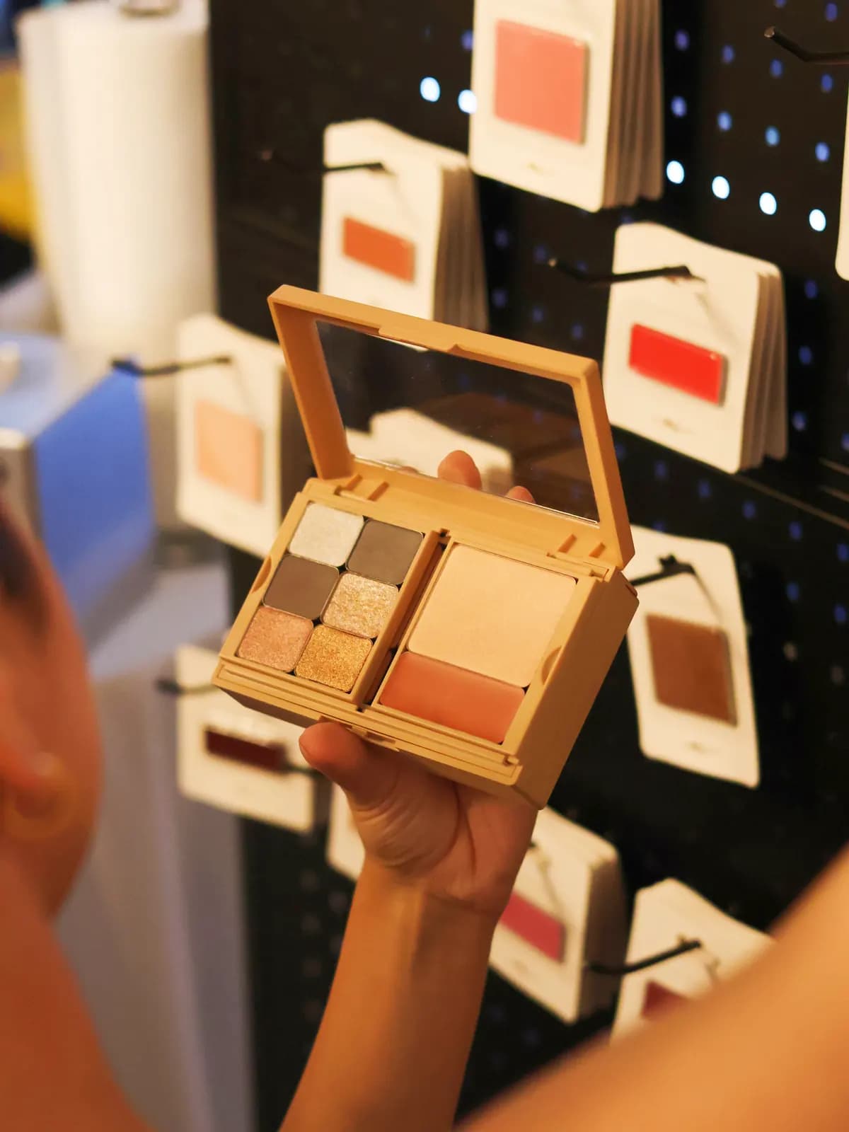A guest holds an open custom MiPalette palette in front of the refill shade display.