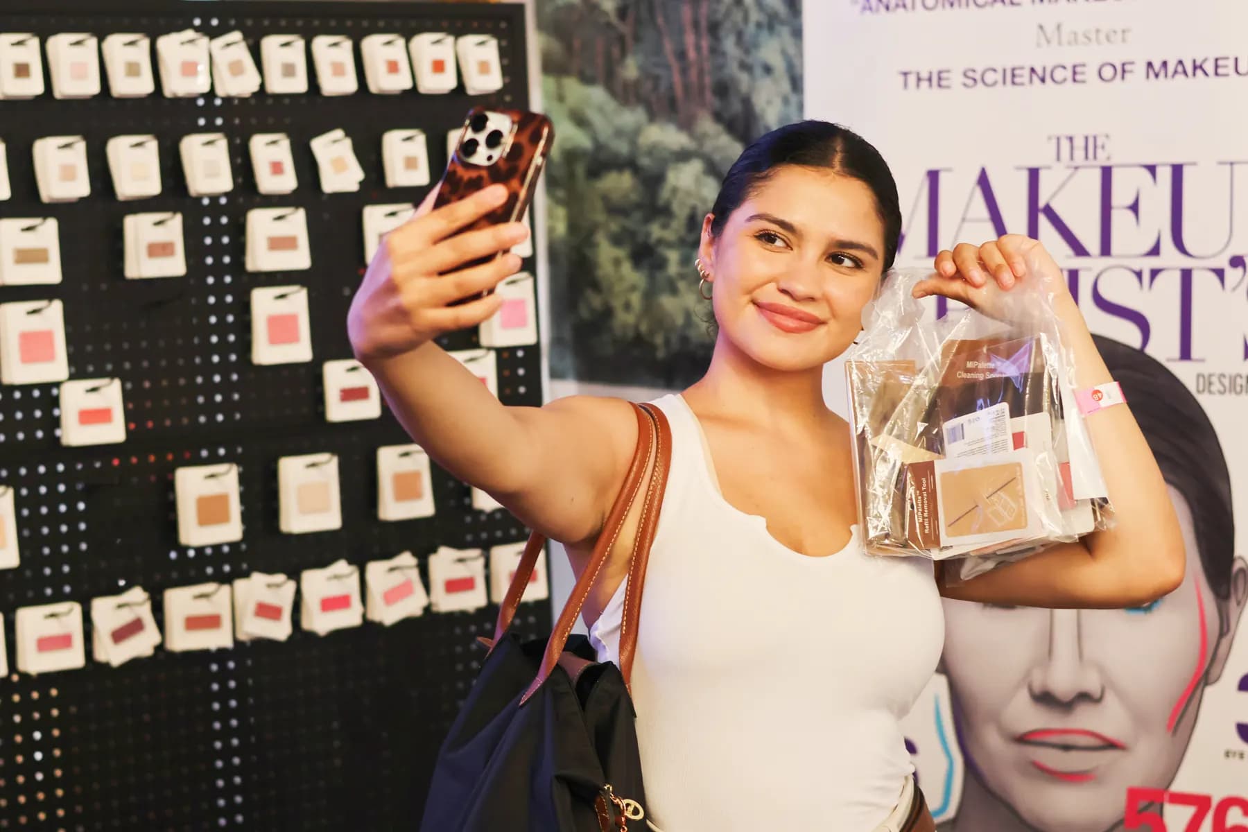 A guest takes a selfie while holding a MiPalette product gift bag beside the shade wall.