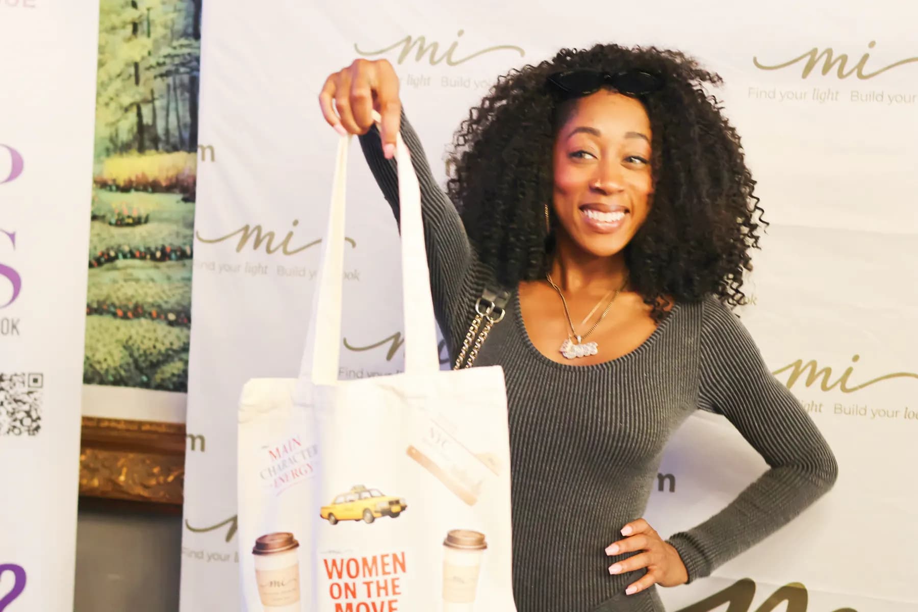 A smiling guest holds up a customized MiPalette event tote in front of the brand backdrop.