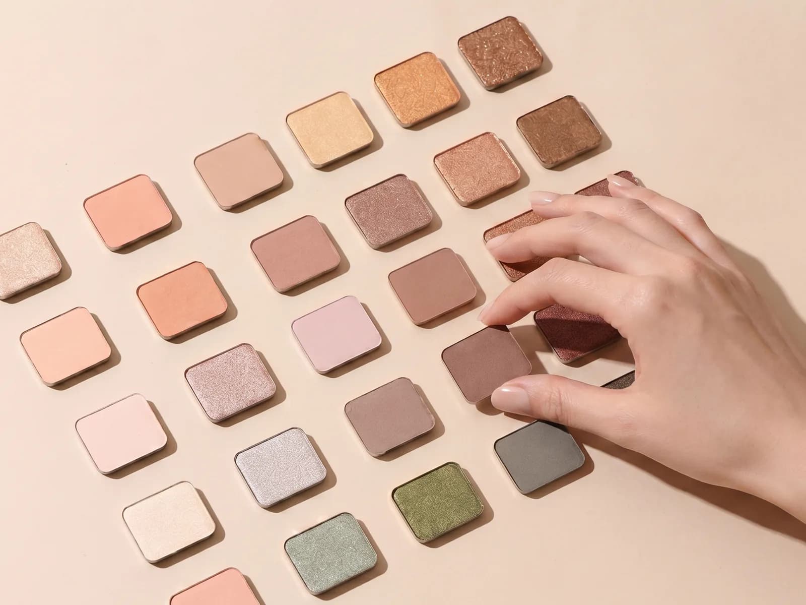 Overhead view of warm-toned makeup pans with a hand picking one