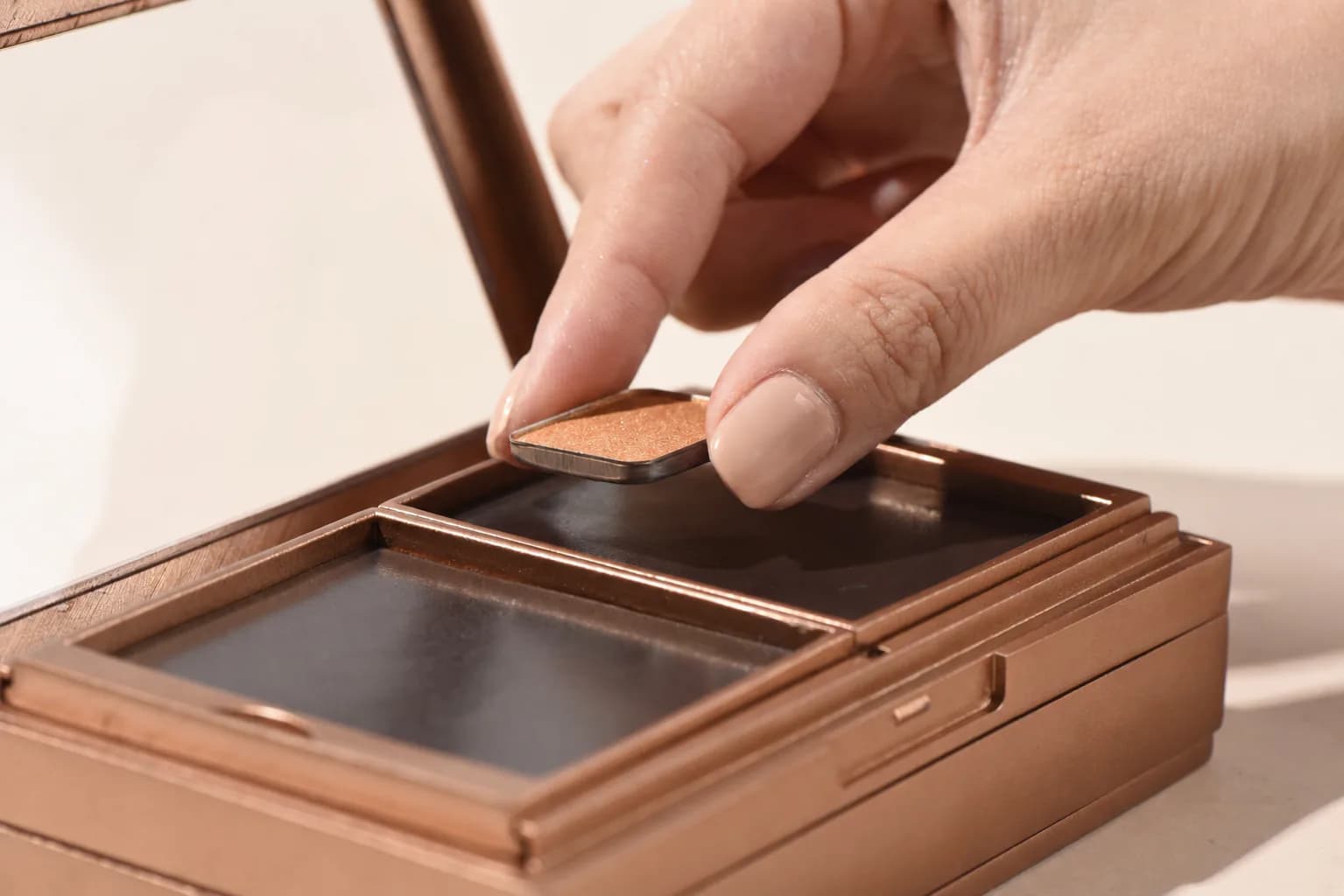 Hand placing a makeup pan into a gold modular case with loose pans scattered nearby